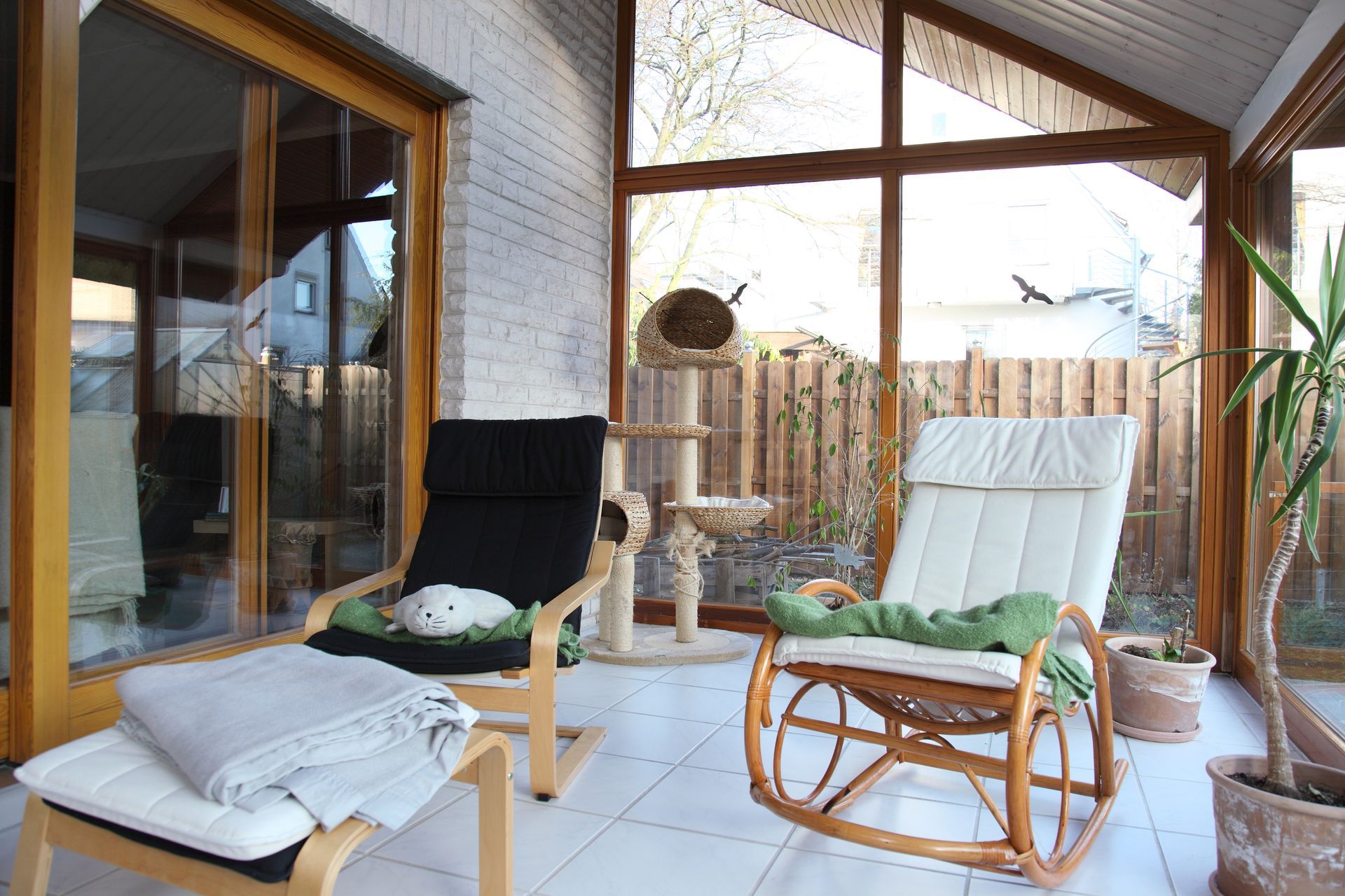 Cozy sunroom with wicker chairs, a cushioned bench, and large windows overlooking a fenced yard