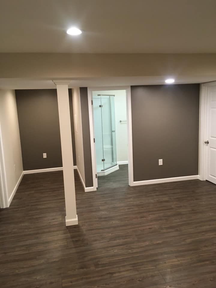An empty basement with hardwood floors and a walk in shower.