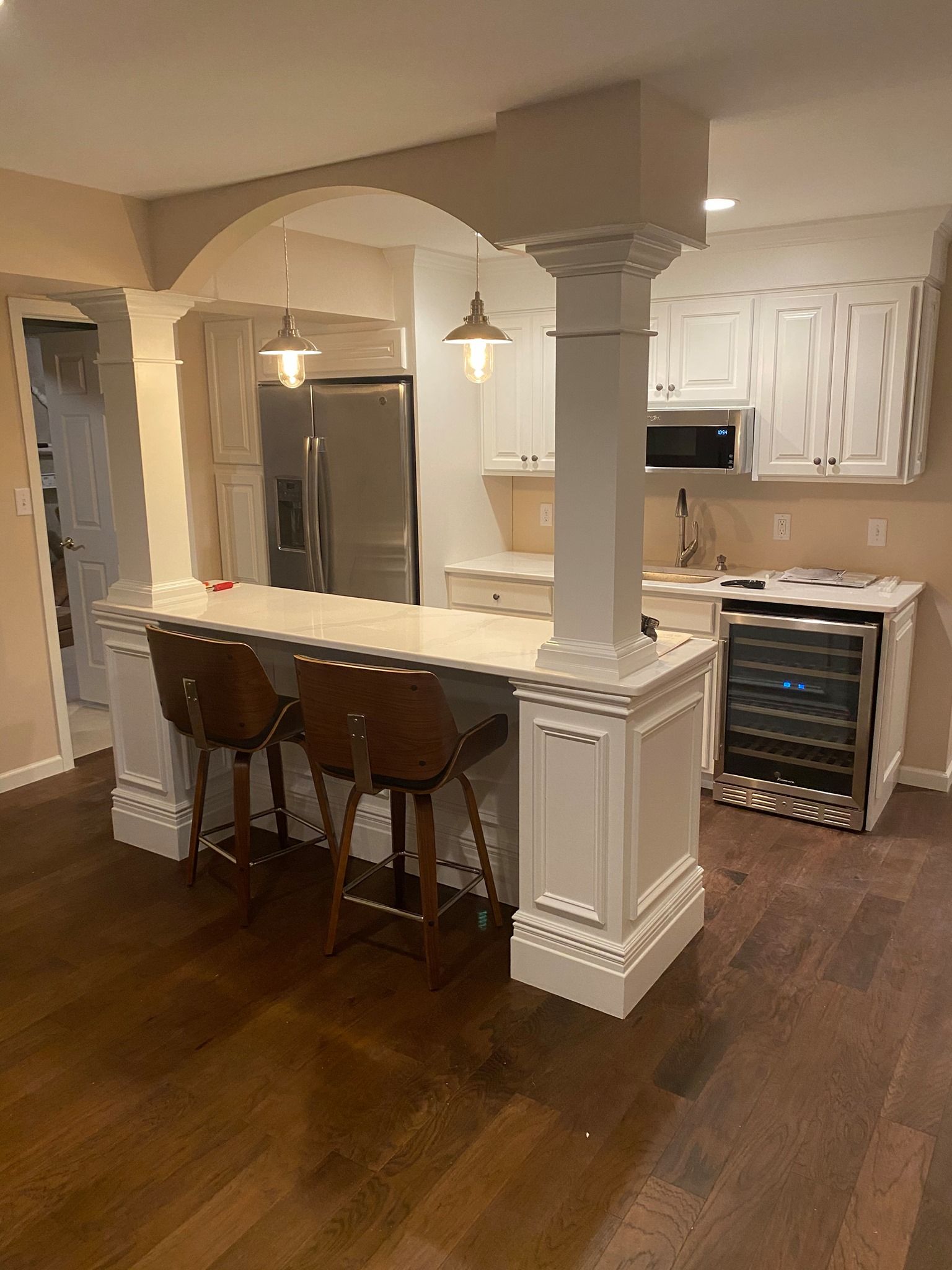 A kitchen with a large island , stools , a refrigerator and a wine cooler.