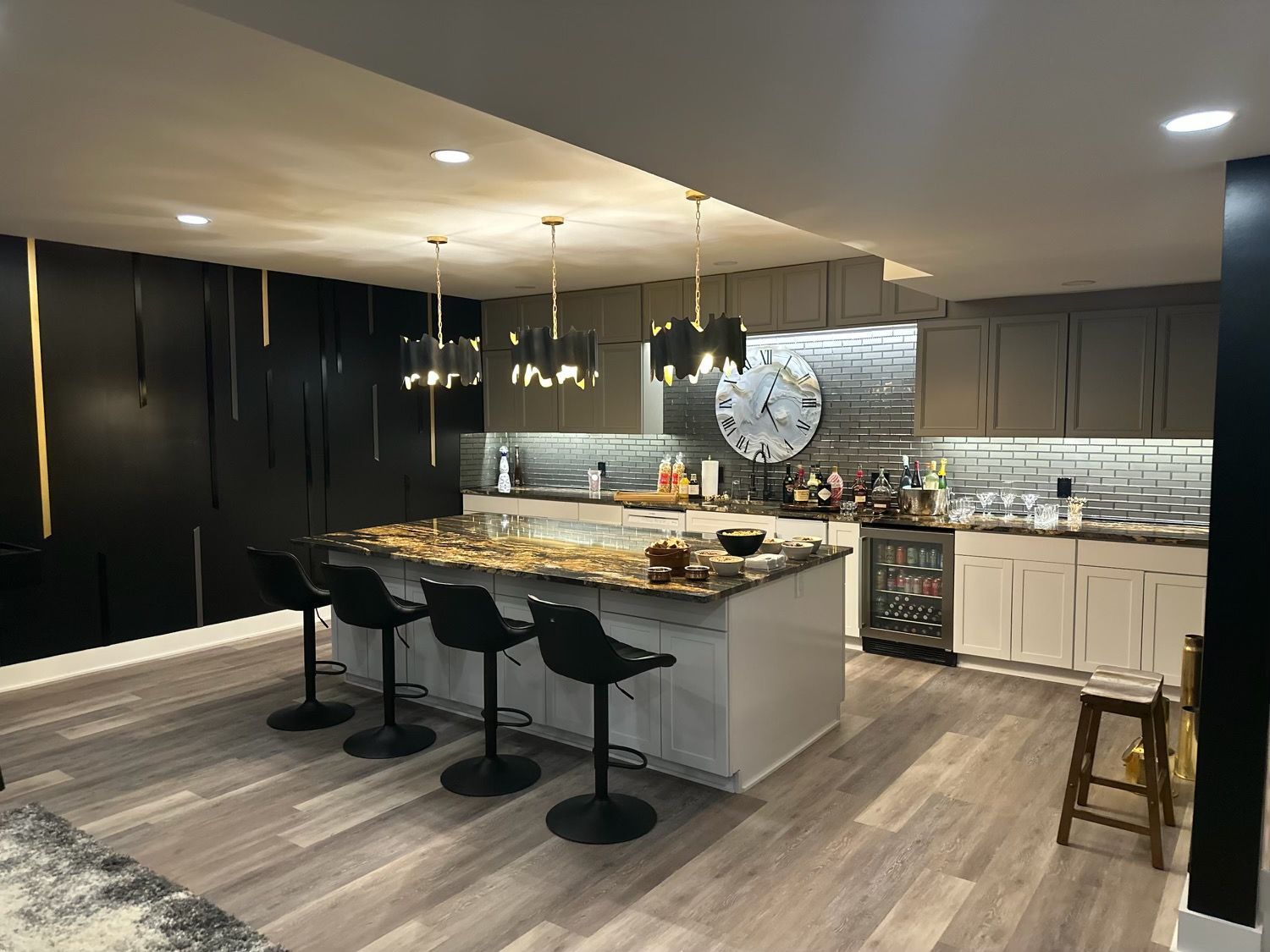 Modern kitchen with an island, black bar stools, unique pendant lights, and a large wall clock.