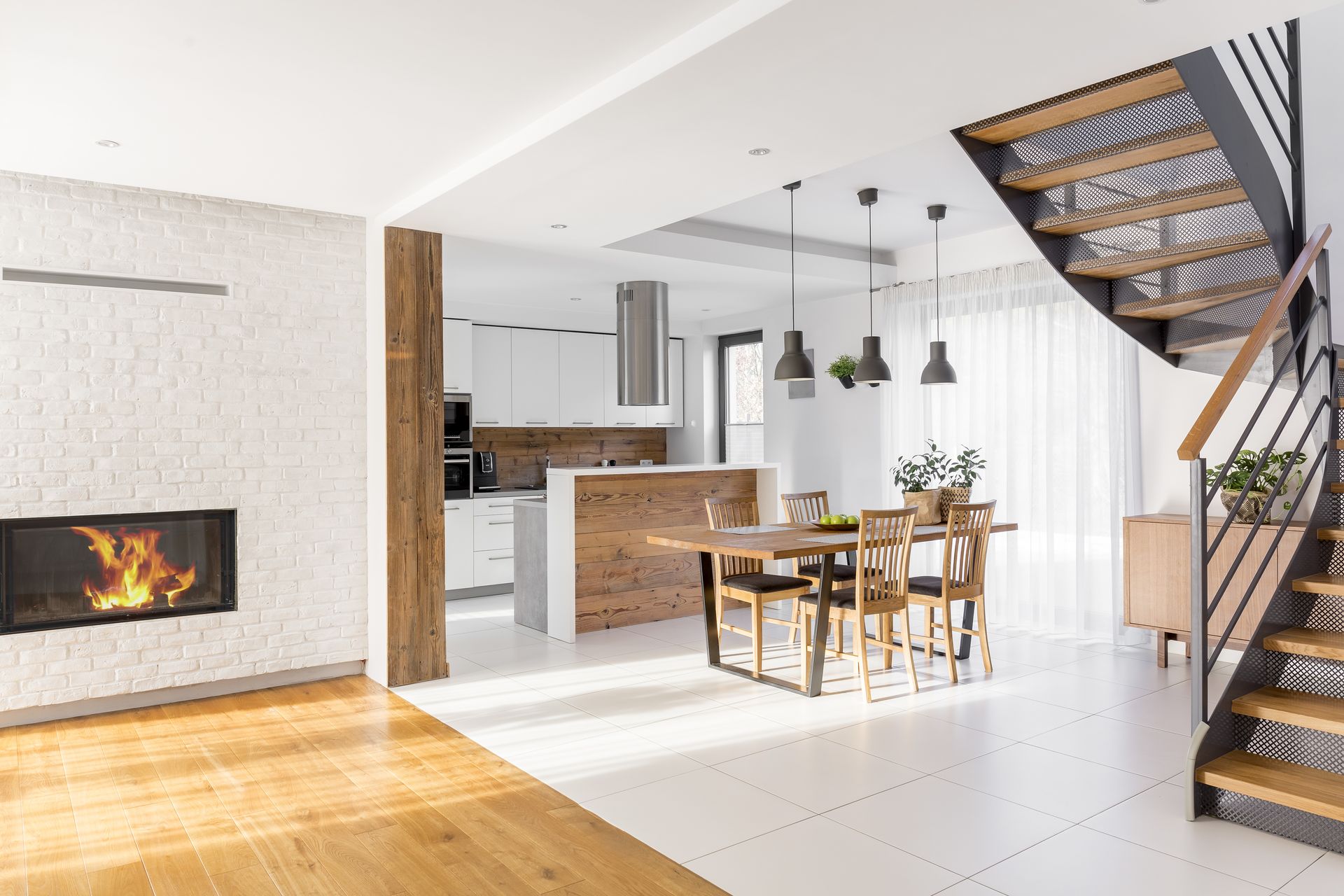 Bright modern open-plan living room and kitchen with staircase, fireplace, and wooden dining table