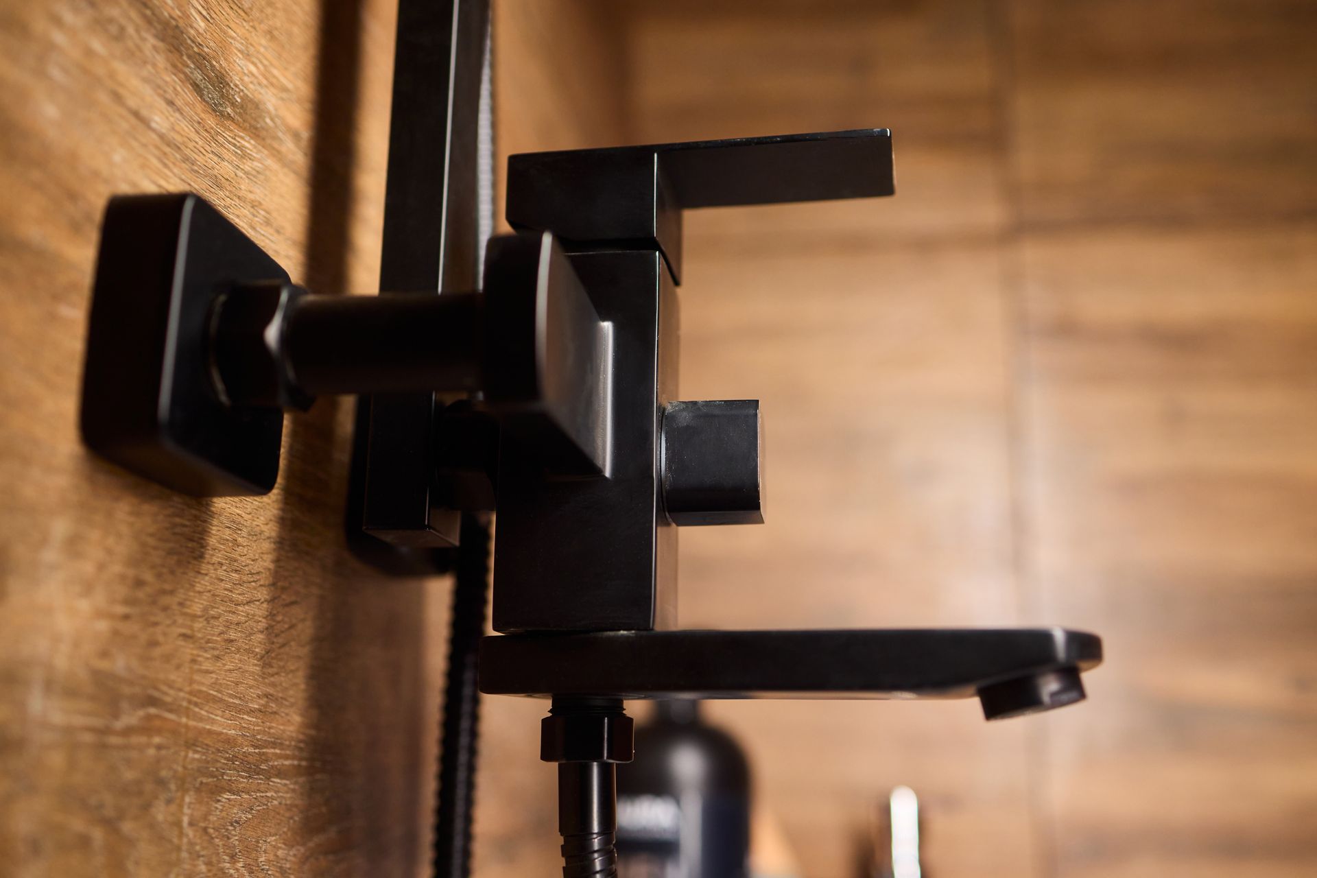 Black metal wall-mounted faucet against a warm wooden bathroom wall.