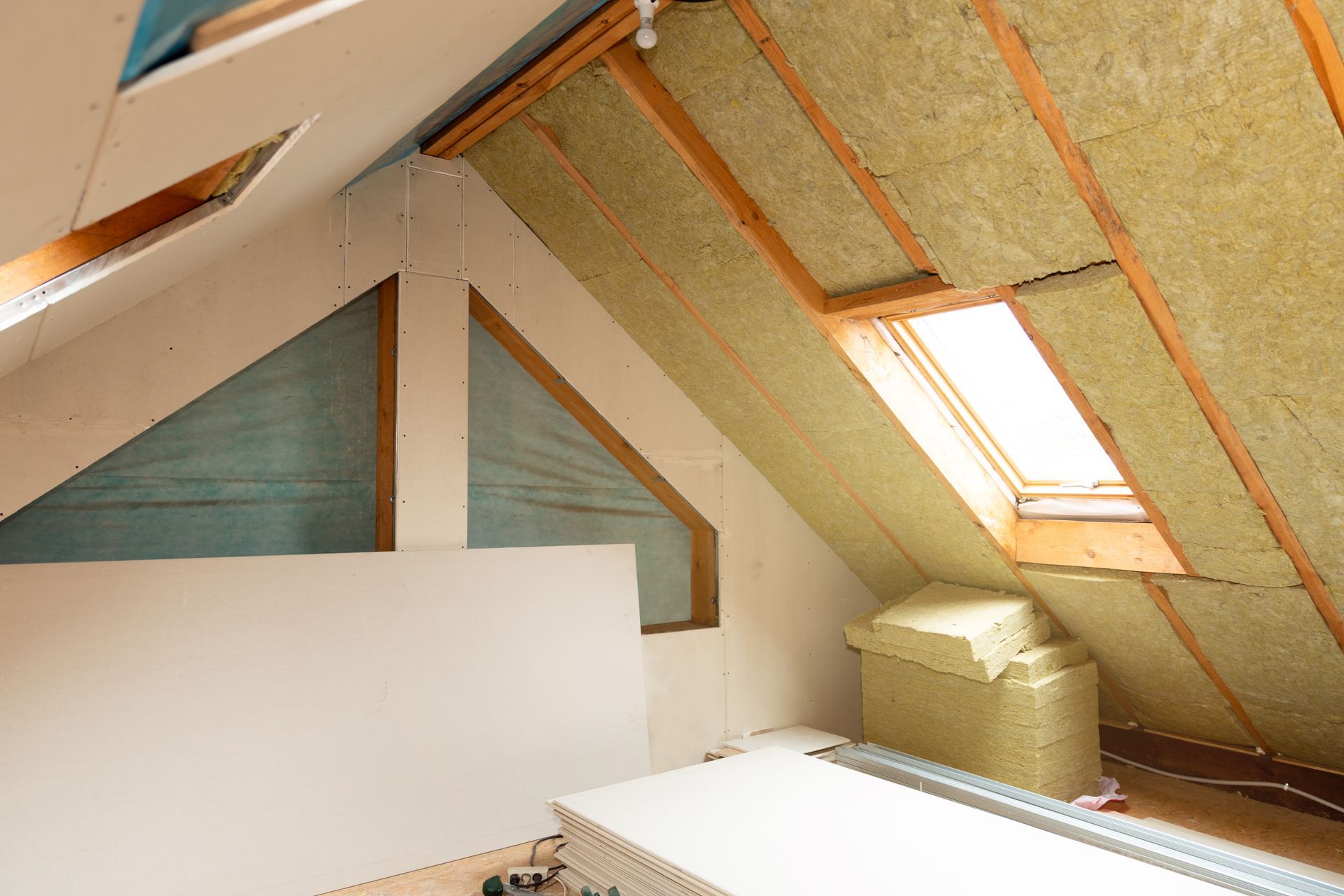 Attic interior with sloped insulated walls, exposed beams, and a skylight window
