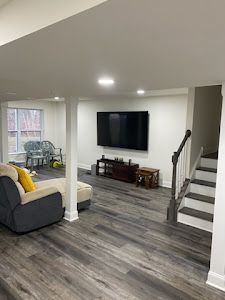 A living room with a couch , chair , television and stairs.