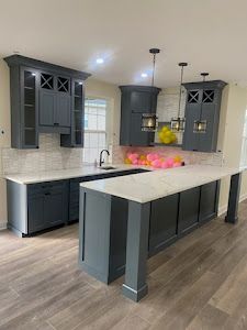 A kitchen with gray cabinets , white counter tops , and a large island.