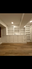 A large empty room with hardwood floors and white cabinets.