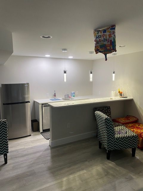 A living room with a refrigerator , chairs , and a balloon hanging from the ceiling.