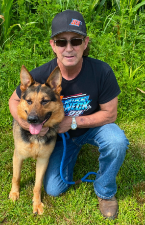 A man is kneeling down next to a german shepherd dog.