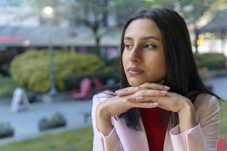 A woman is smiling with her eyes closed in a park.