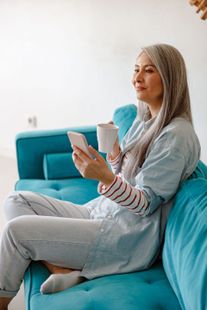 A woman is smiling with her eyes closed in a park.