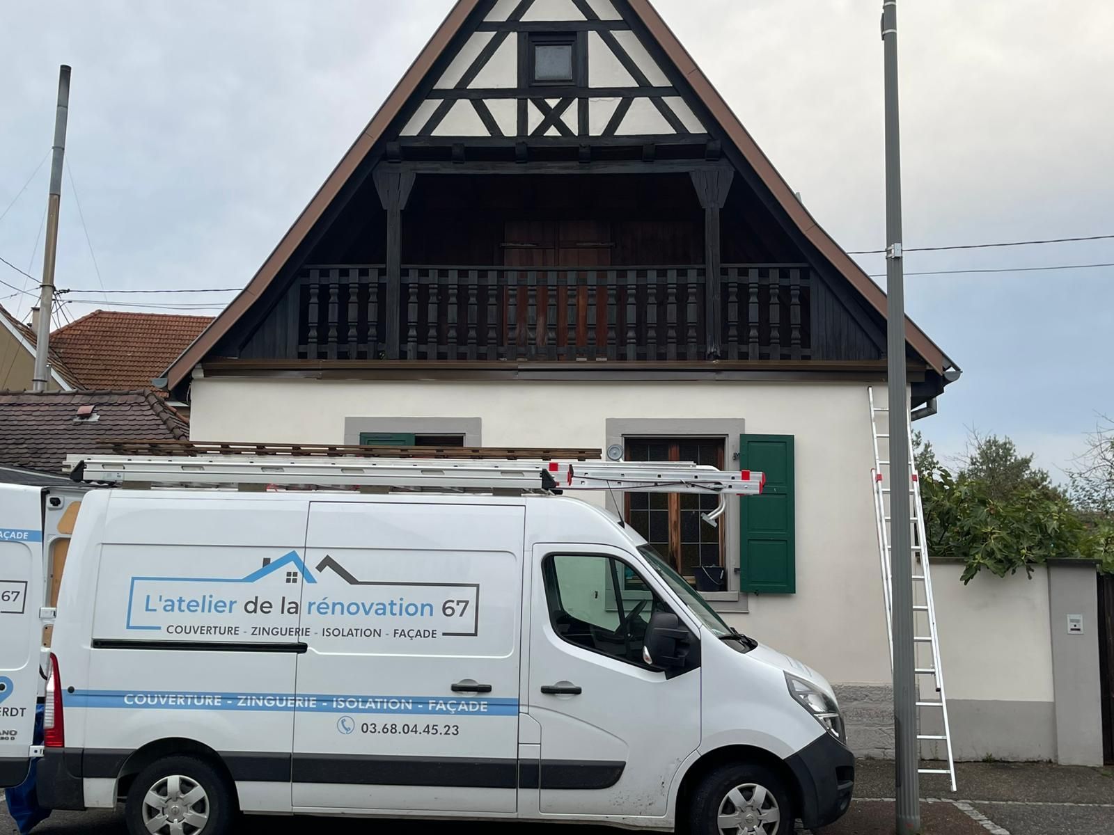 Une camionnette blanche arborant le logo d'une entreprise est garée devant une maison à colombages ; une échelle est appuyée contre le mur.