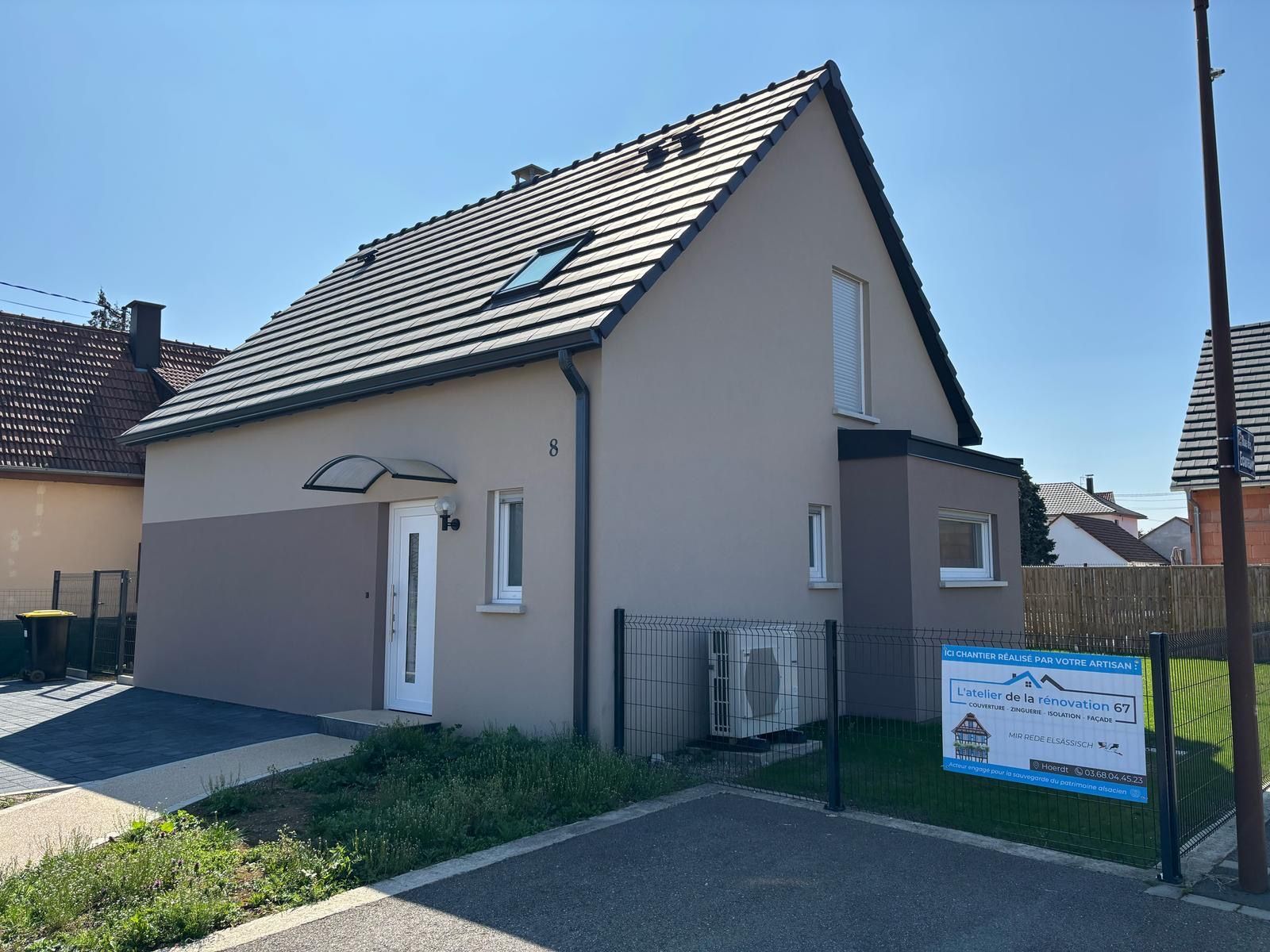 Maison beige au toit foncé et à la petite cour, par une journée ensoleillée.