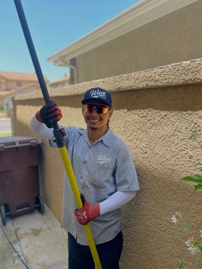 Man in work uniform holding a long pole near a building.