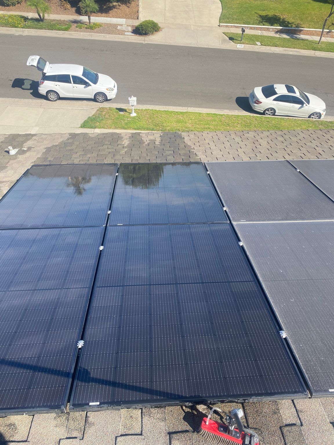 Solar panels on a roof, reflecting sunlight. Cars parked on street below.