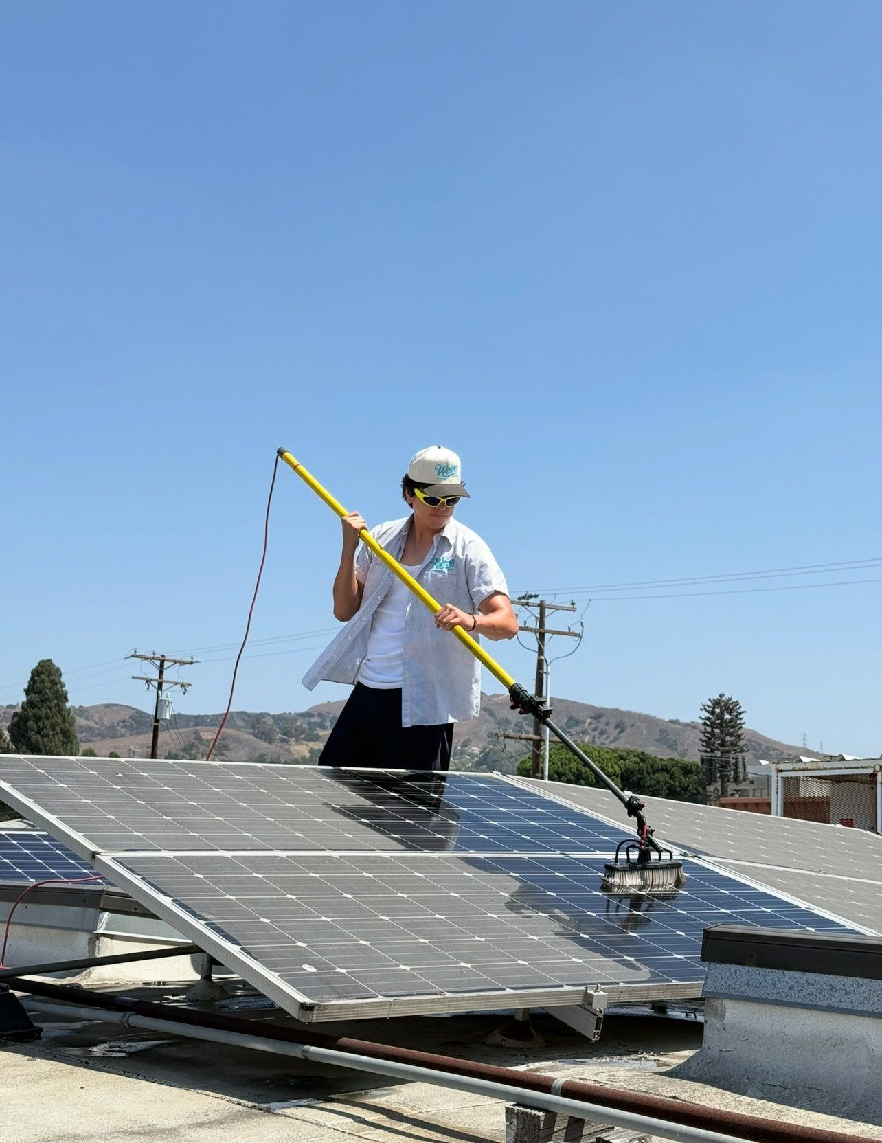 Solar panels being cleaned with a long-handled brush, on a wet, reflective rooftop.