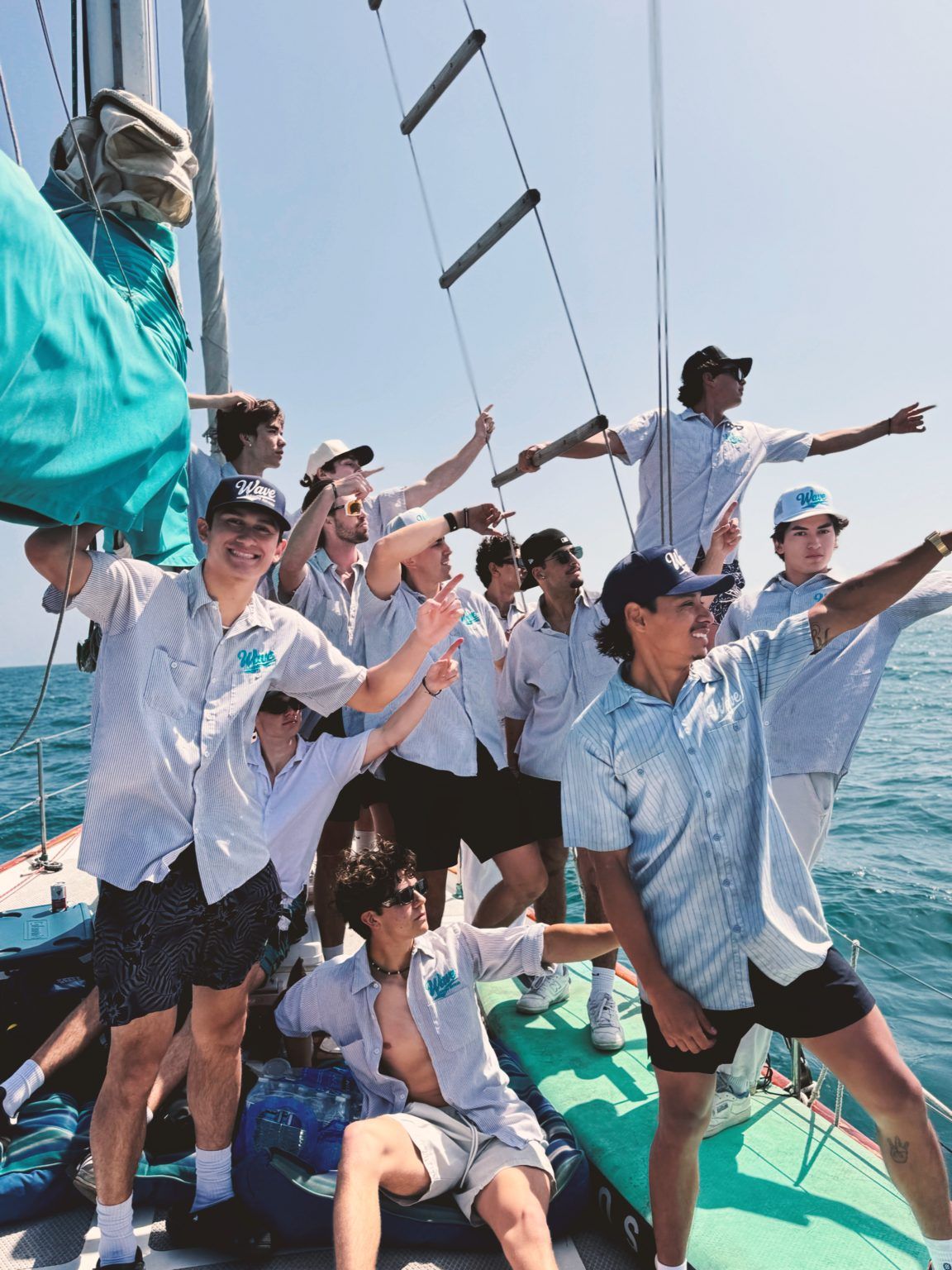 Group of people on a sailboat, pointing towards the sea on a sunny day.