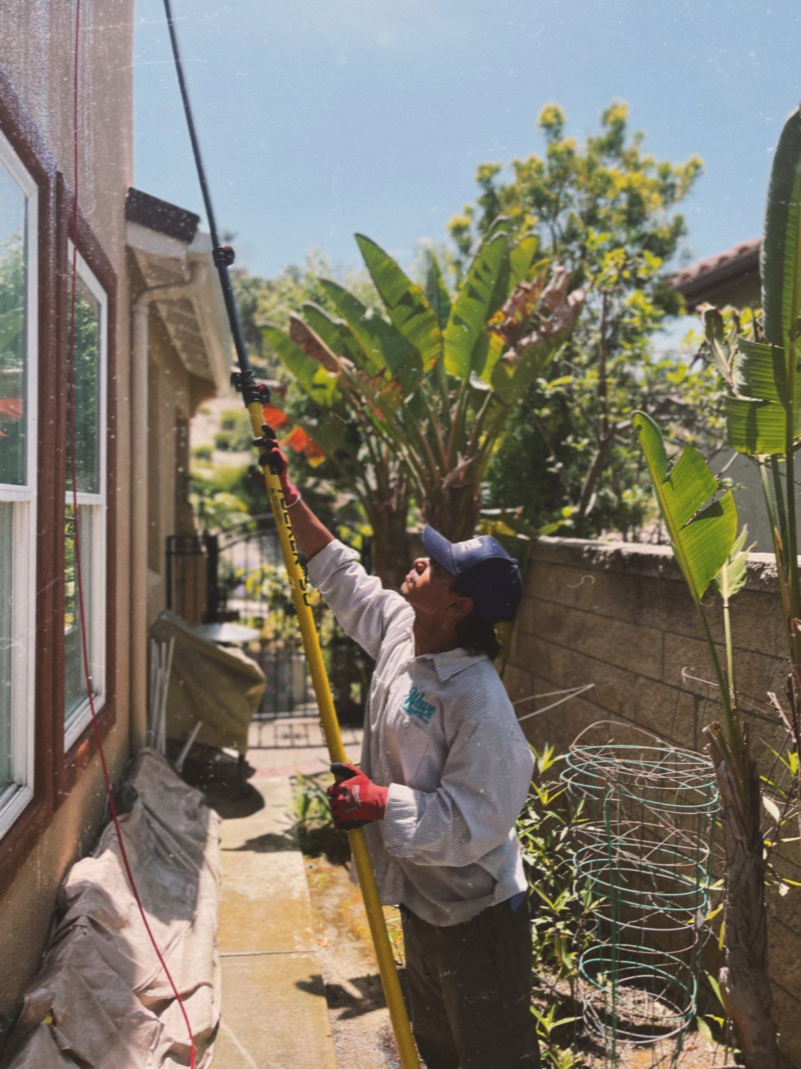 Person using a pole to wash a window on a house. Bright, sunny day.