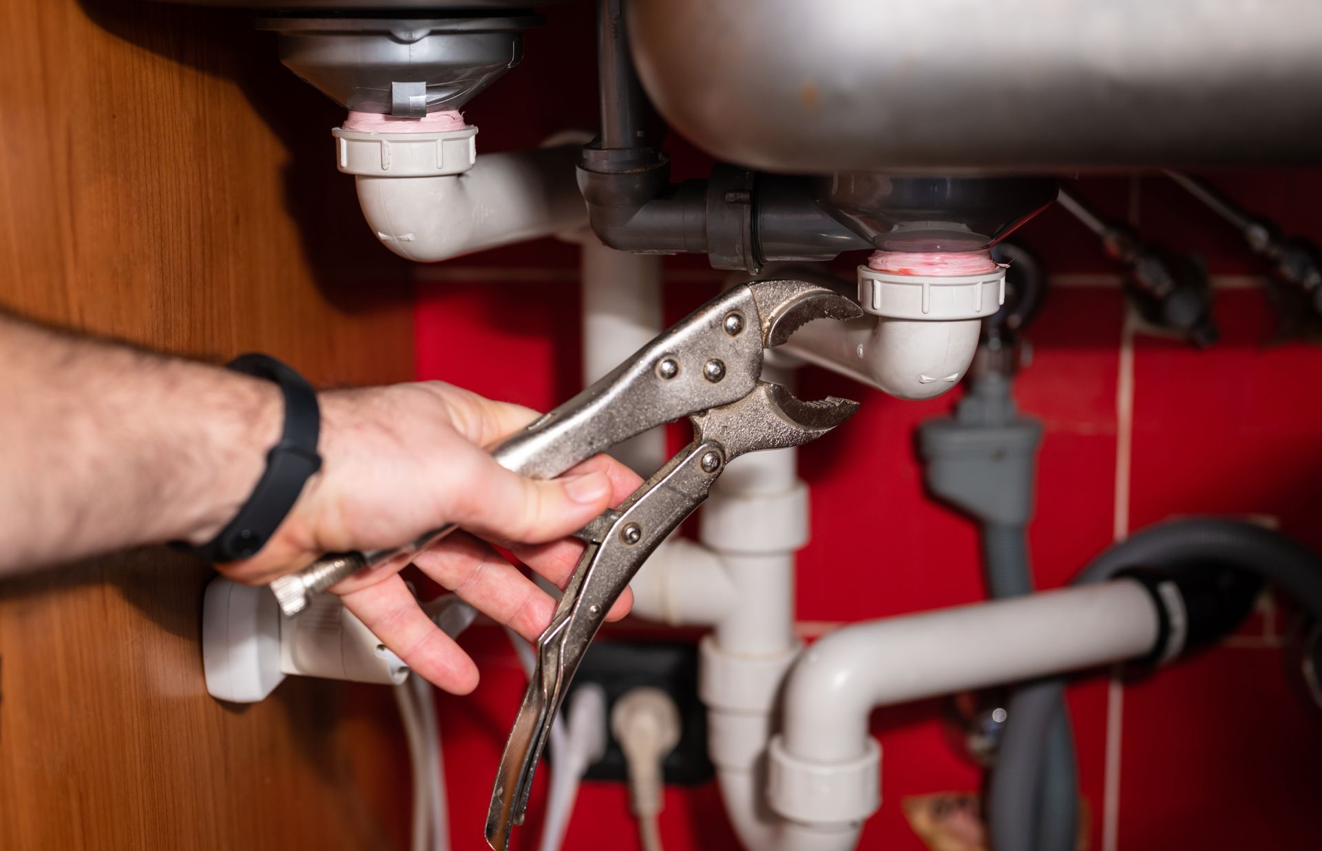 Hand holding pliers, working on pipes under a sink.