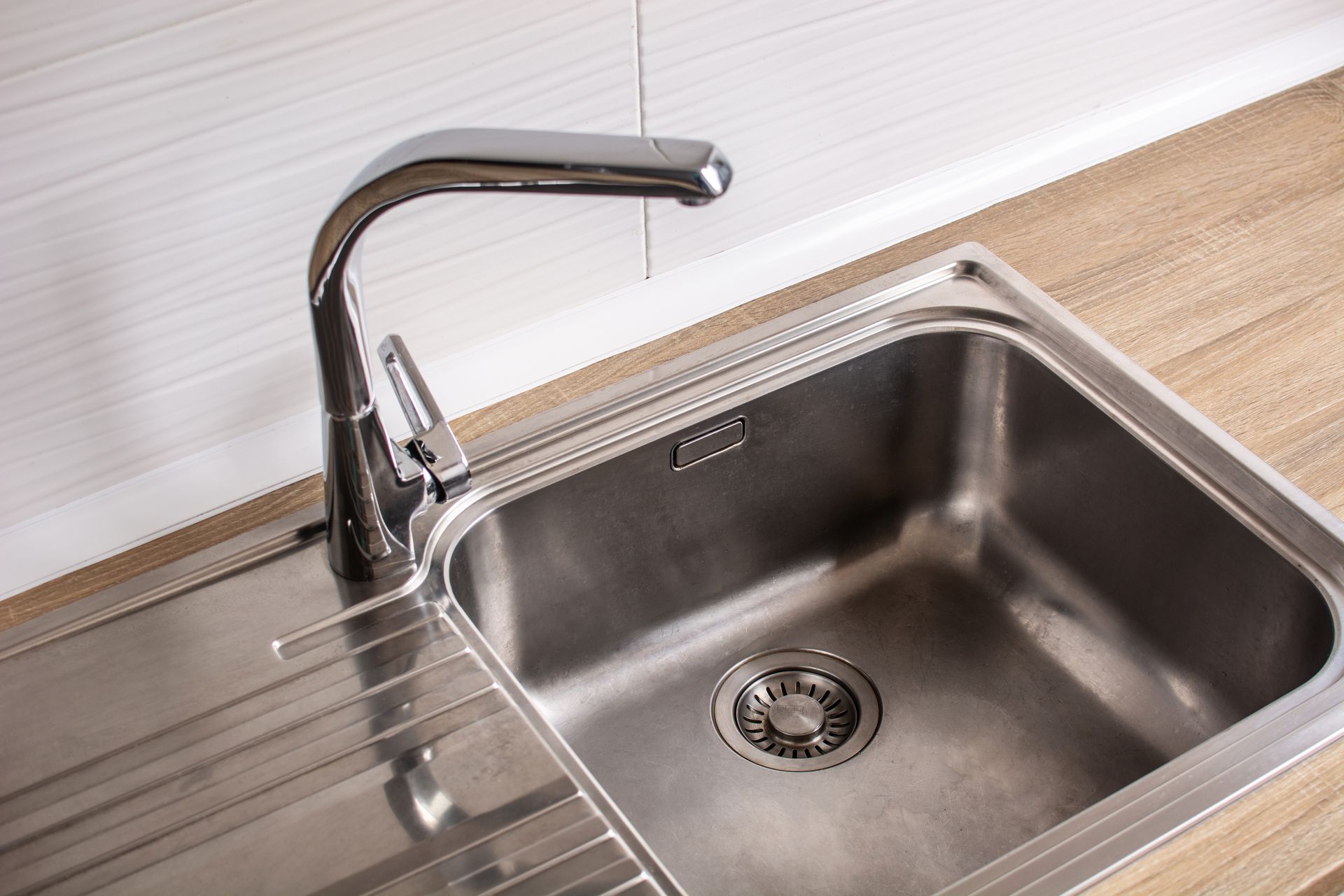 Stainless steel kitchen sink with faucet, set in a wooden countertop, white wall in background.