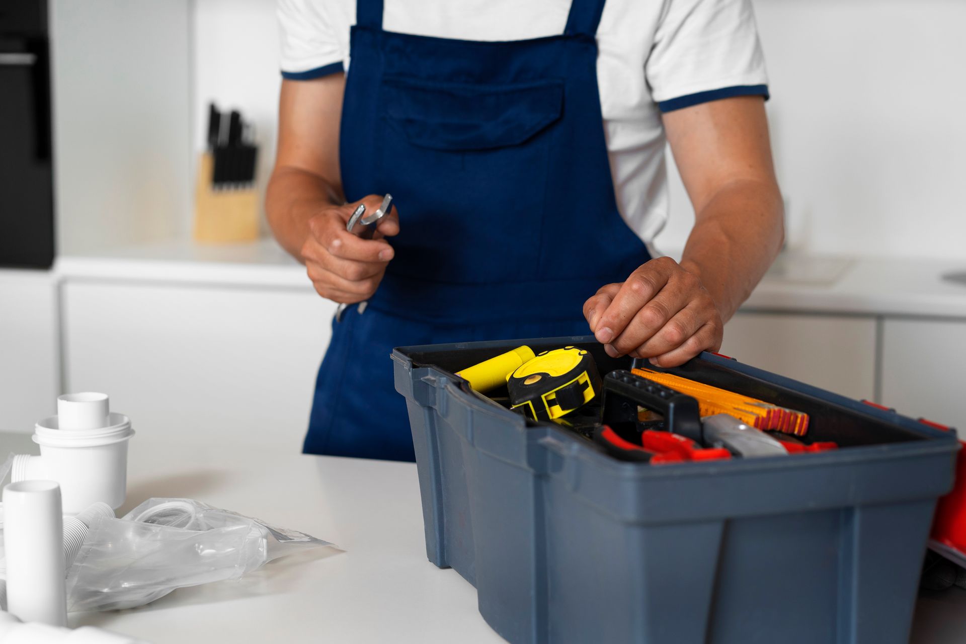 Person in blue apron selecting a tool from a toolbox in a kitchen.
