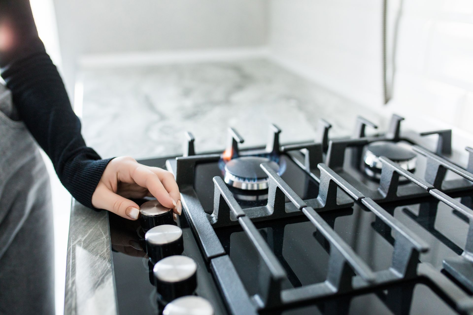 Person turning a knob on a black gas stovetop in a bright kitchen