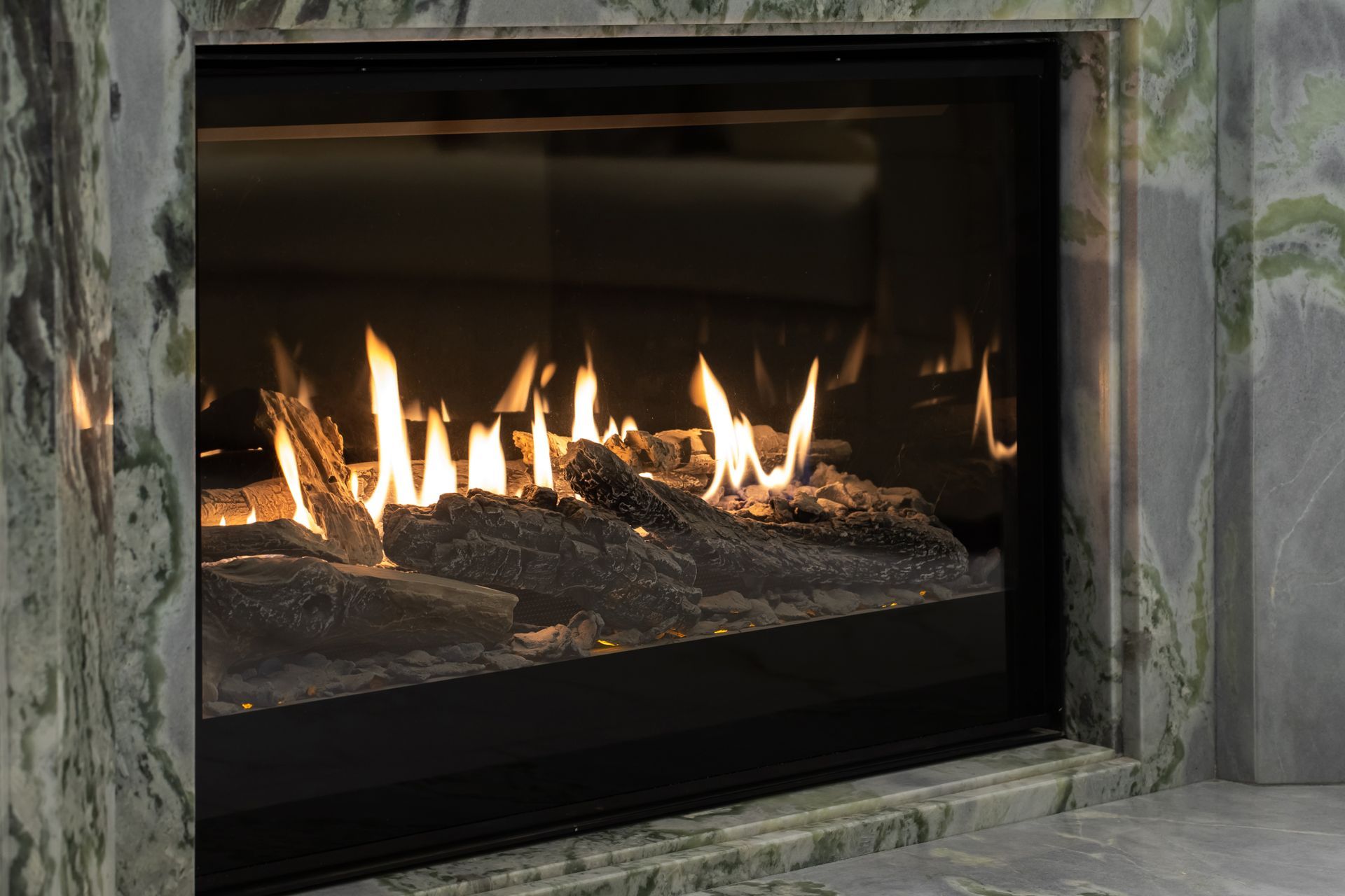 Modern gas fireplace with bright flames behind a glass panel in a stone surround