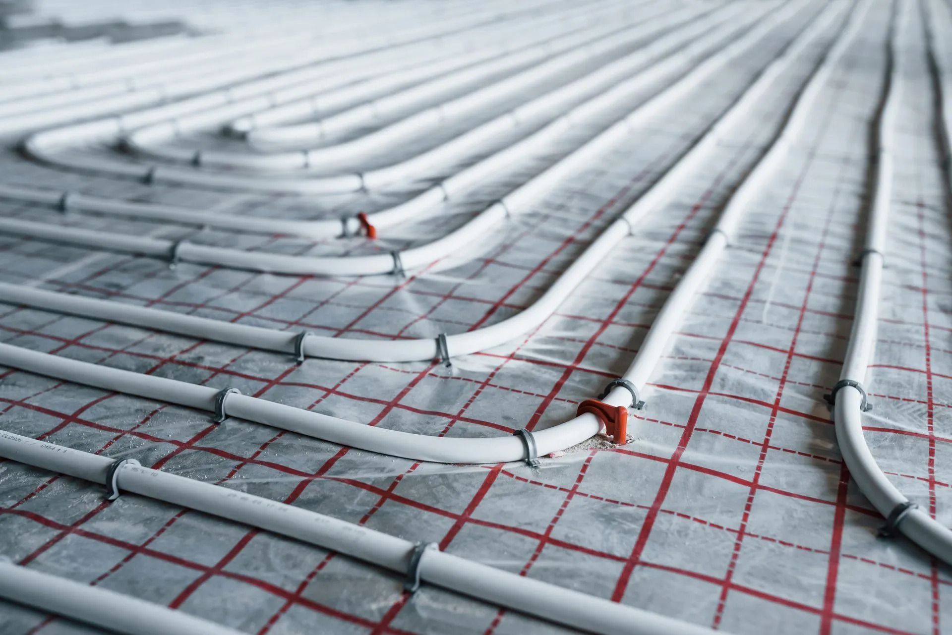 Gray coiled tubing on a red grid over a rooftop underlayment with small connection points