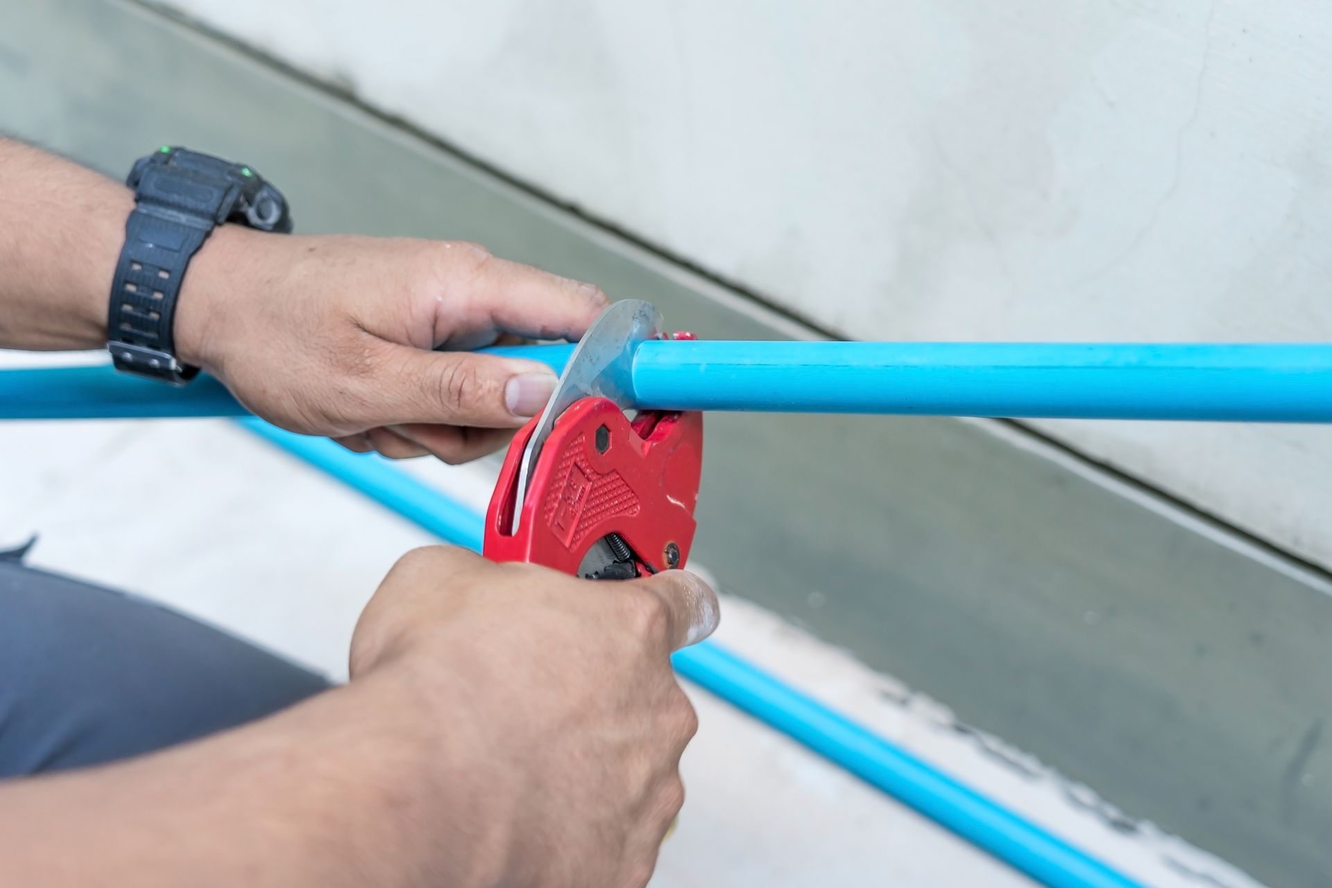 Hands using a red pipe cutter on a blue PVC pipe indoors