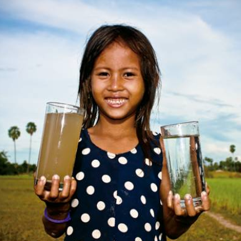 A young girl is holding two glasses of water in her hands