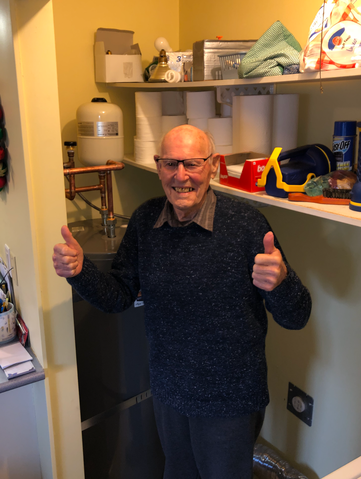 An elderly man is giving a thumbs up in a laundry room