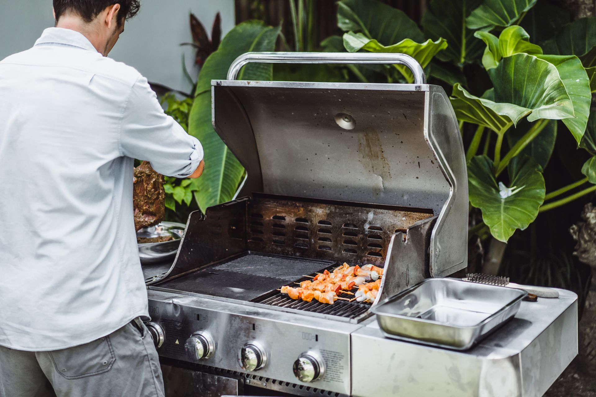 A man is cooking shrimp on a grill outside.