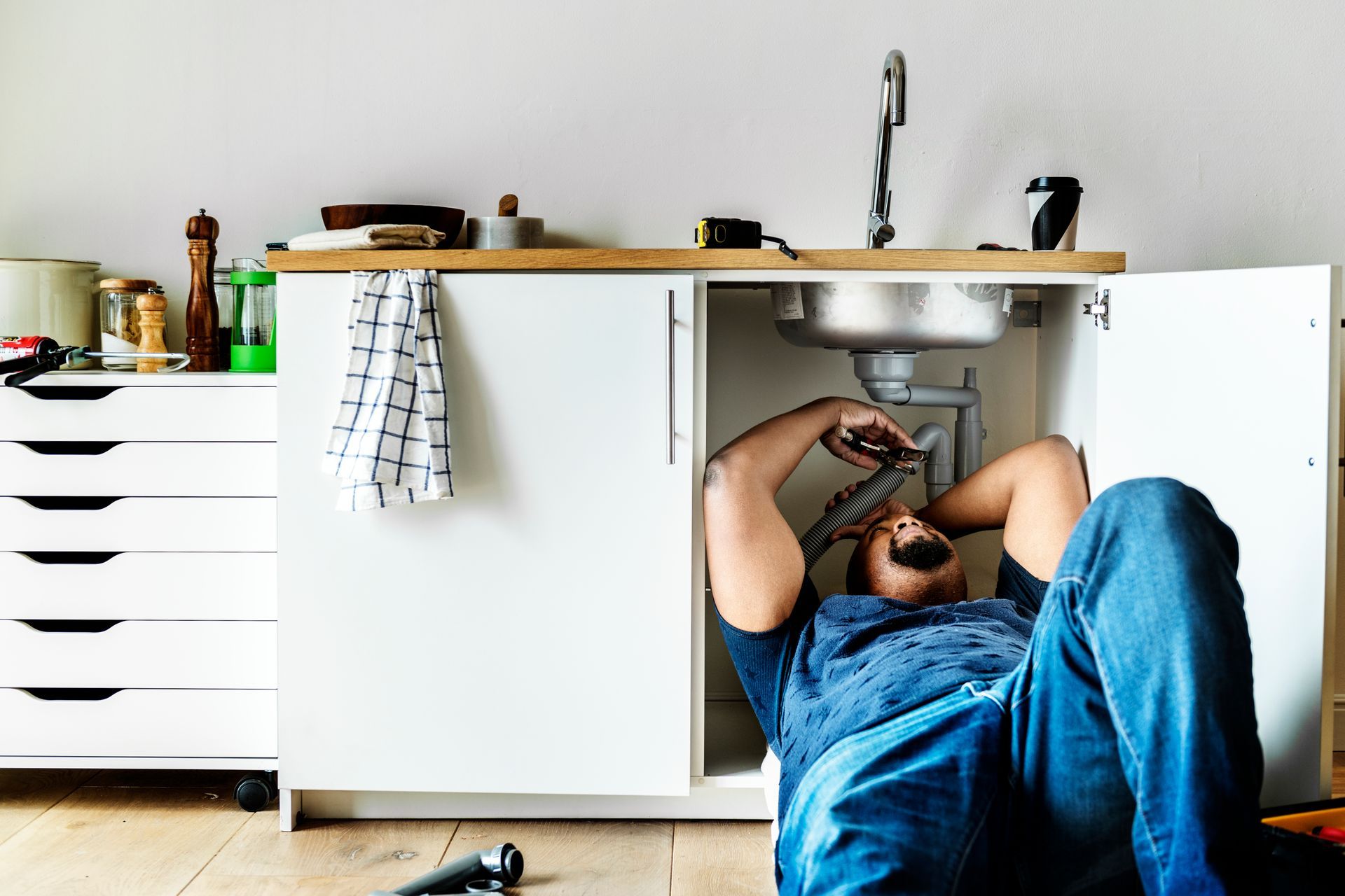 A man is laying on the floor fixing a sink in a kitchen.