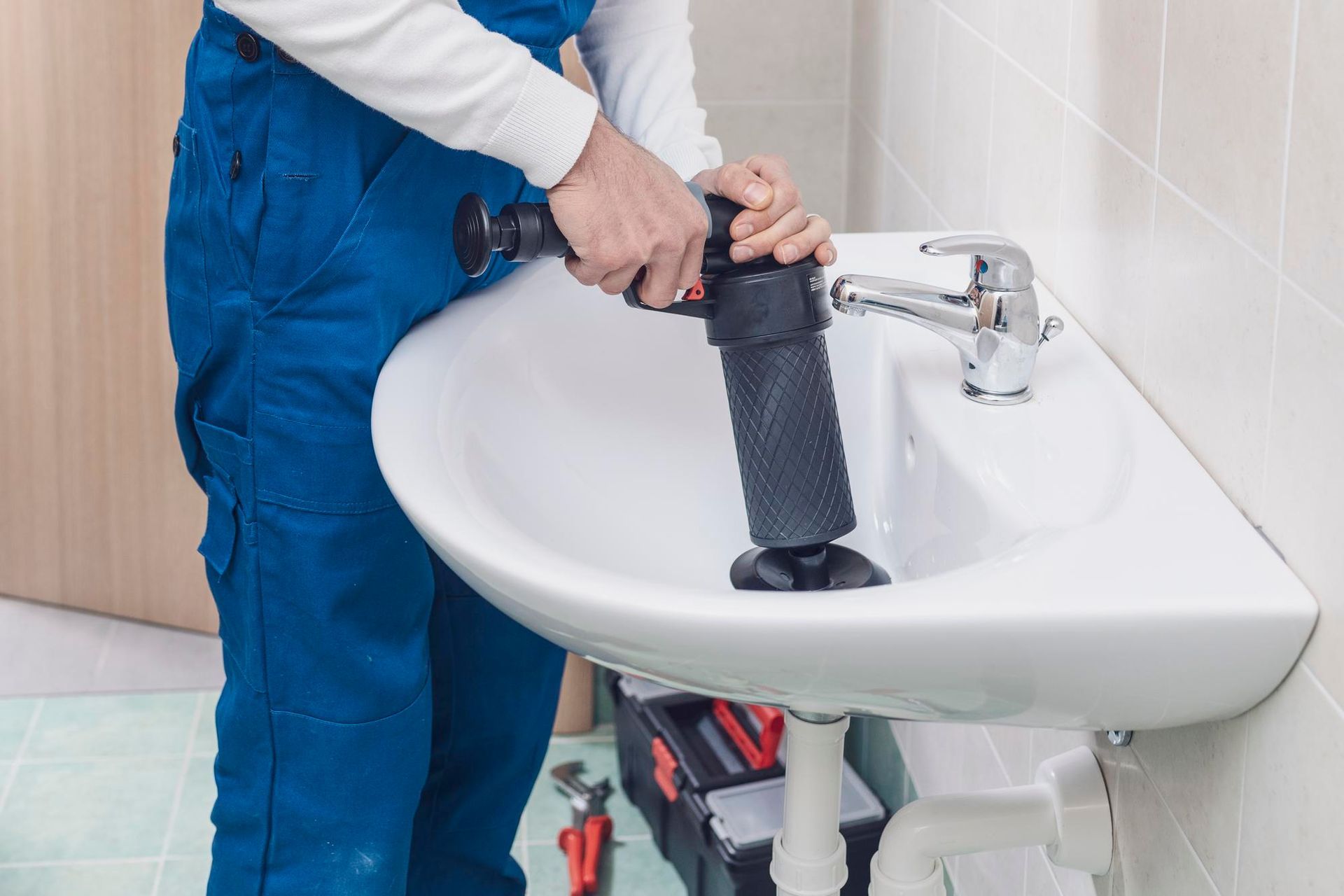A plumber is using a plunger to unblock a sink in a bathroom.