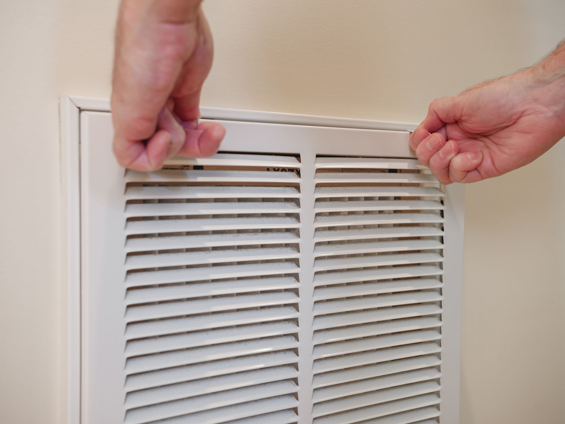 A person is opening a white air vent on a wall.