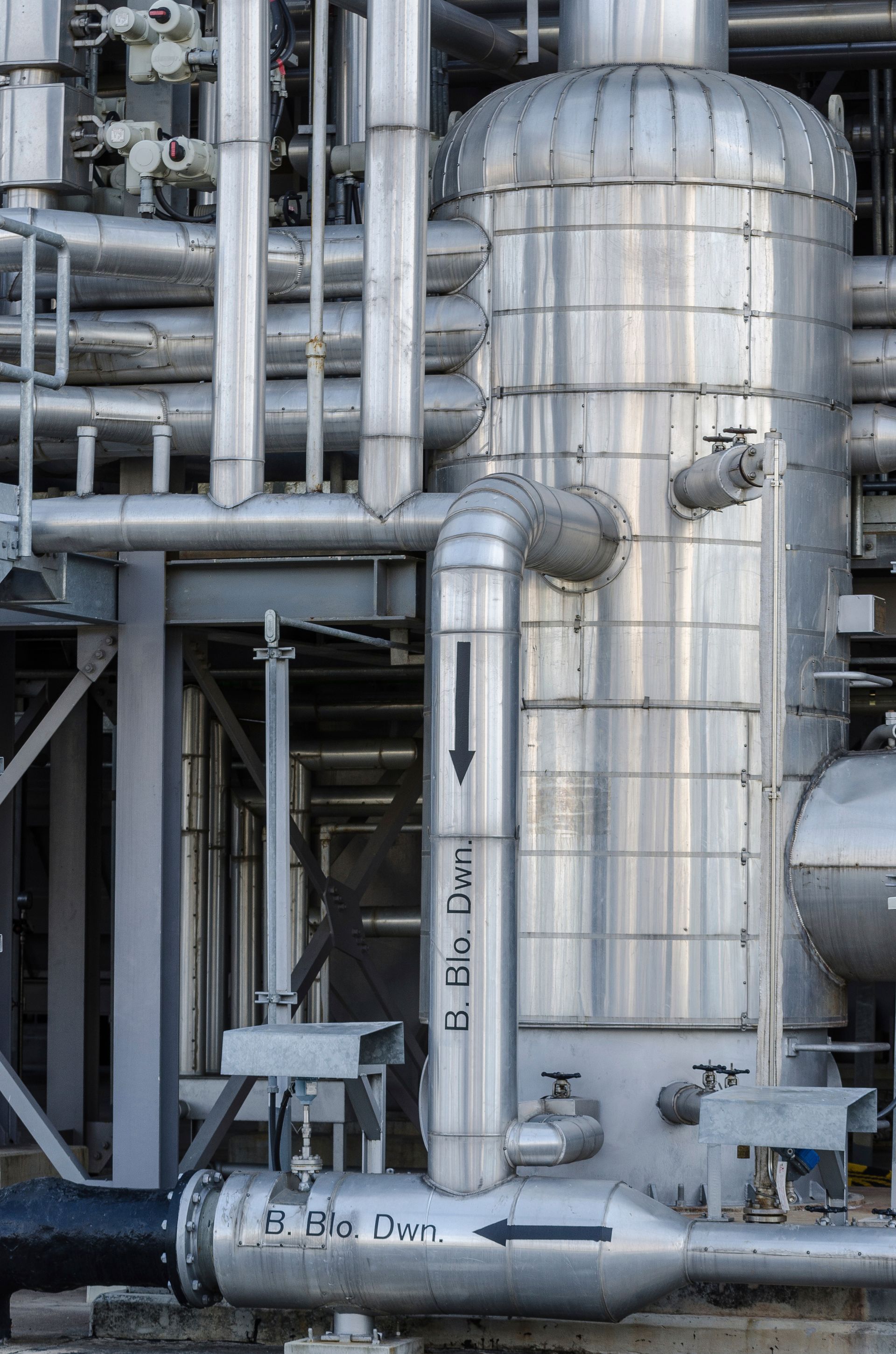 Industrial piping and large silver metal tanks in a factory setting