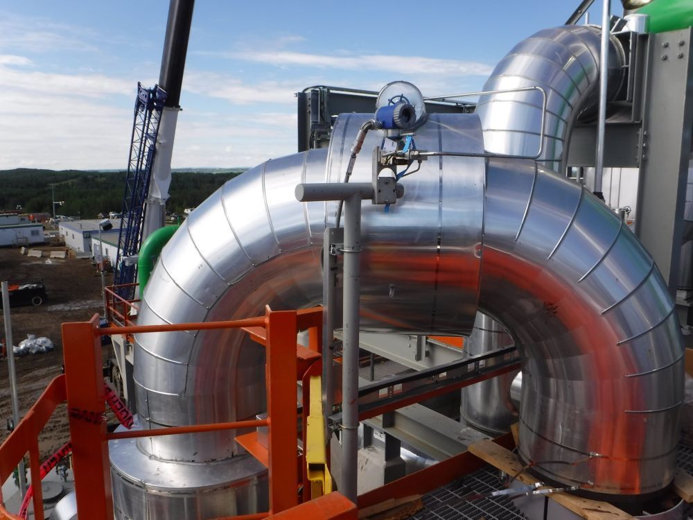 Large silver industrial pipes and ducts at a construction site under a blue sky.