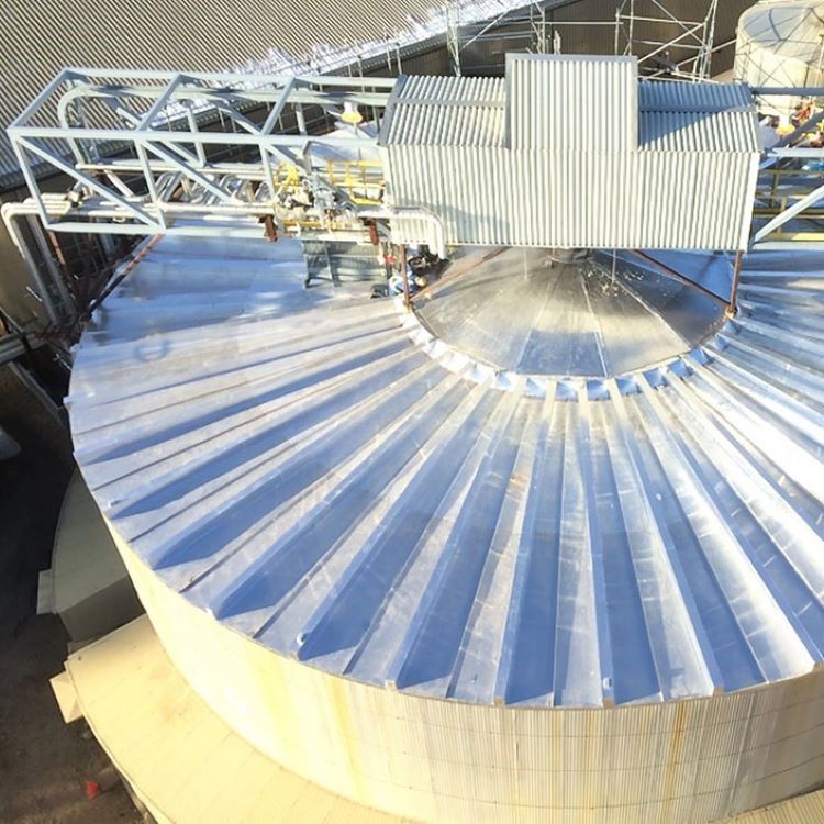 Aerial view of a large silver corrugated storage tank with rooftop machinery and a metal catwalk.