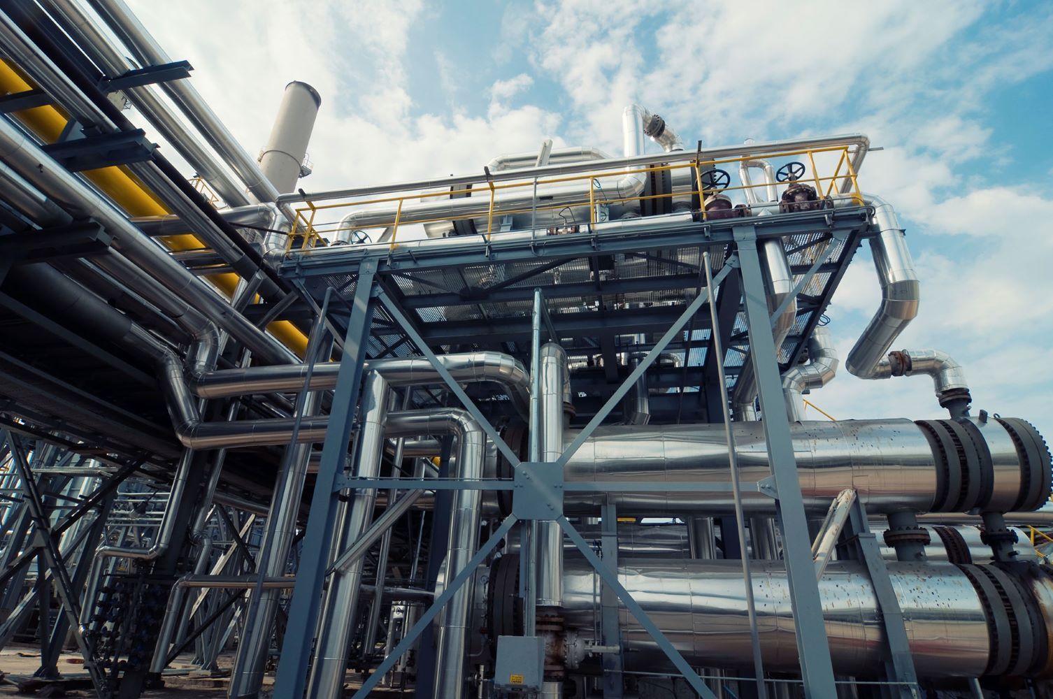 Industrial piping and steel framework at a refinery under a blue sky