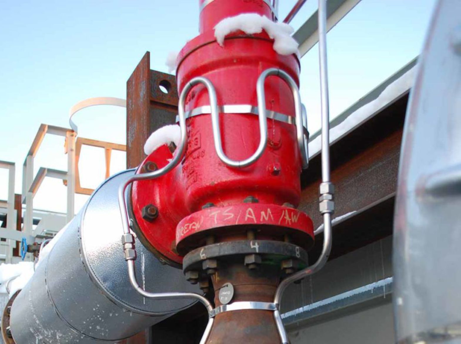 Red industrial fire valve with pipes and snow on an outdoor rooftop platform