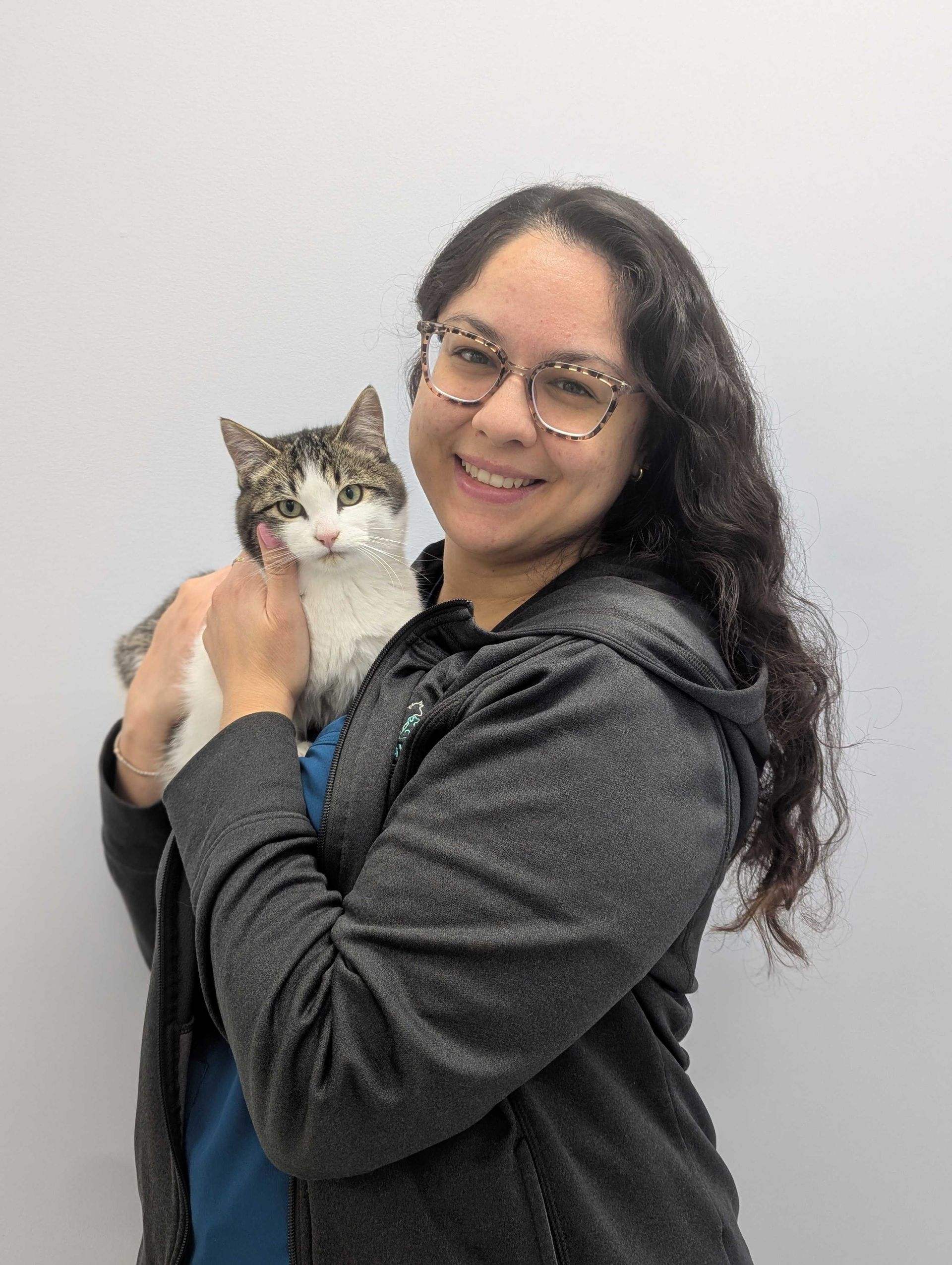 Woman with glasses smiles while holding a cat; both against a white background.