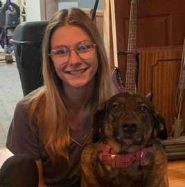 Woman with glasses and dog sitting together; both smiling.