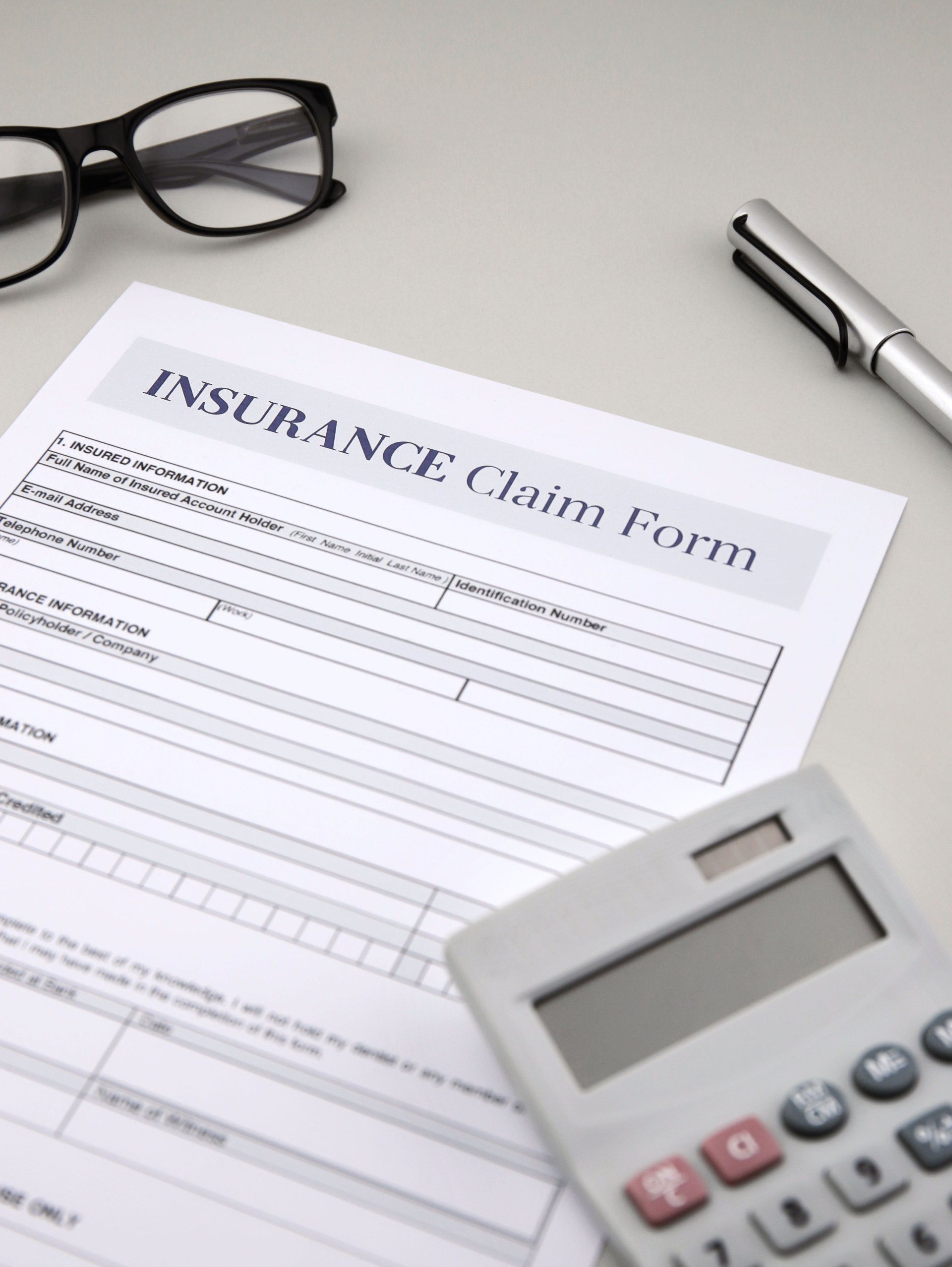 An insurance claim form is on a table next to a pen and calculator