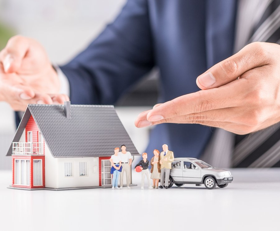 A man is shaking hands over a model house and car.