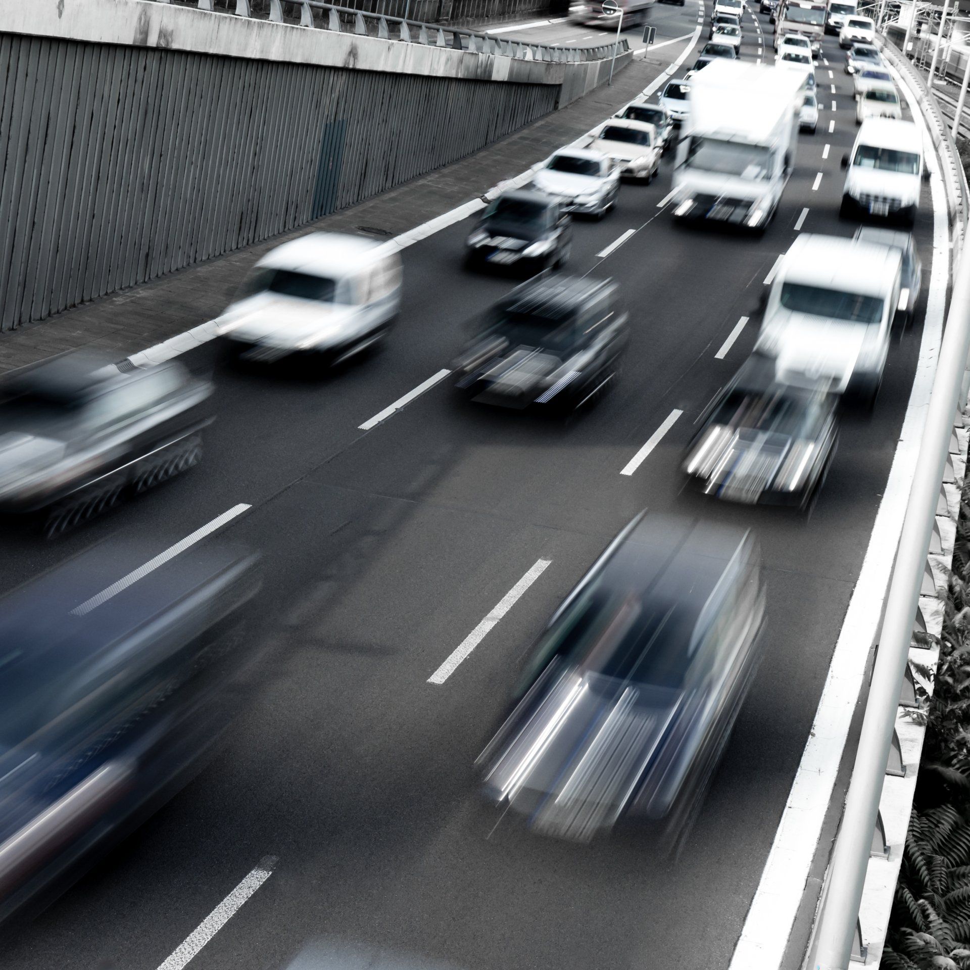 Cars driving on a multi-lane highway, appearing blurred due to motion; a concrete wall is visible on the left.