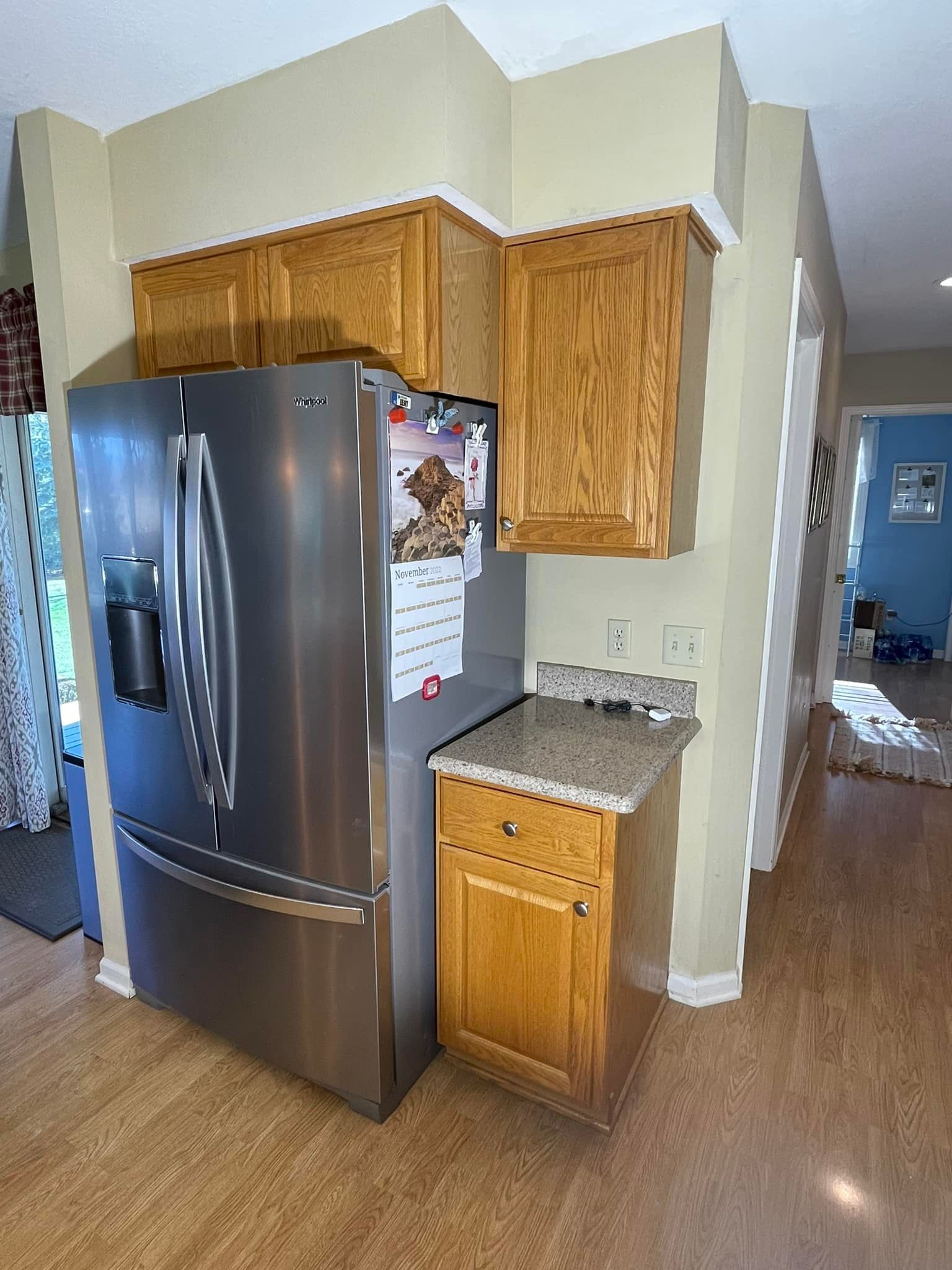 Stainless steel refrigerator in a kitchen with wooden cabinets and a small counter.