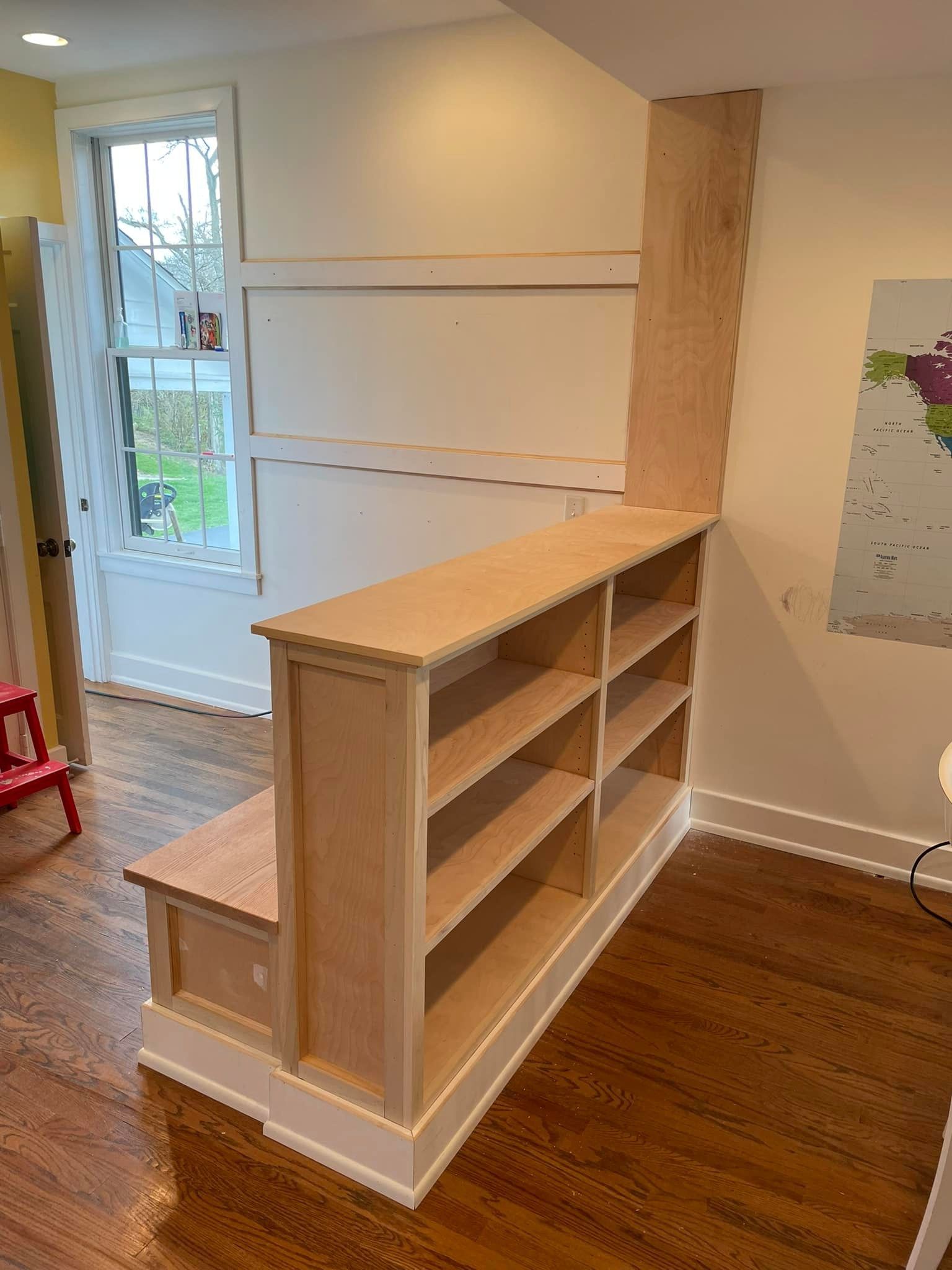 Built-in bookshelf with steps, attached to wall, unfinished wood and white trim, doorway to the left.
