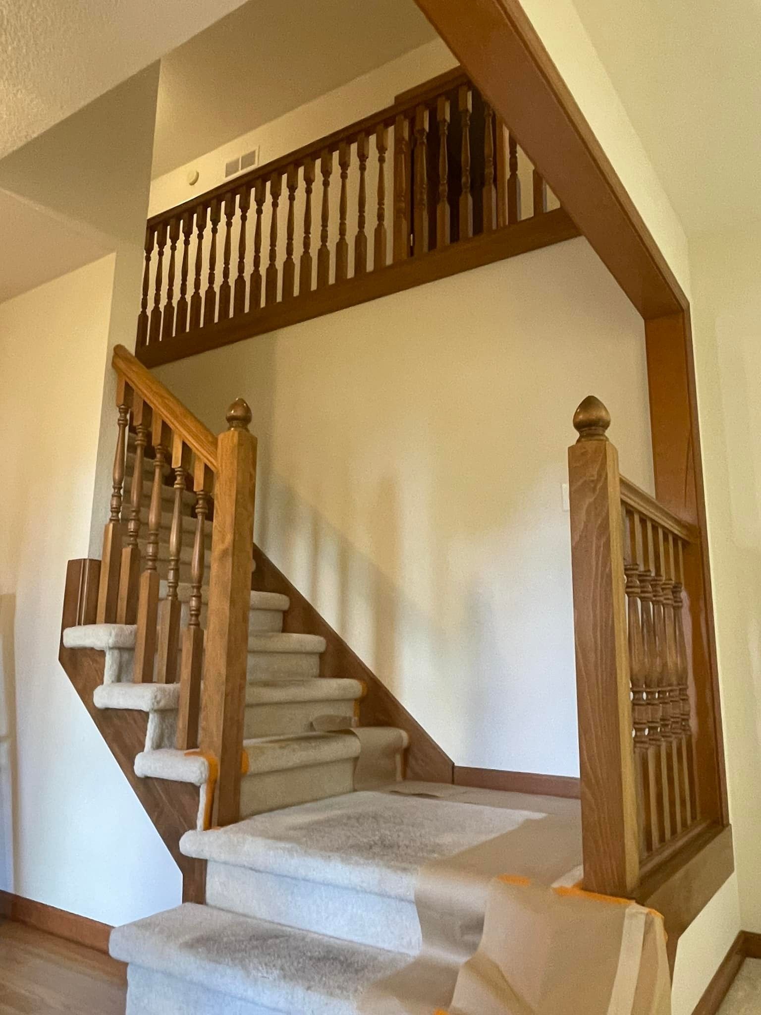 Staircase with wooden banisters leading up to a landing. Carpeted steps, cream walls, and wood trim.