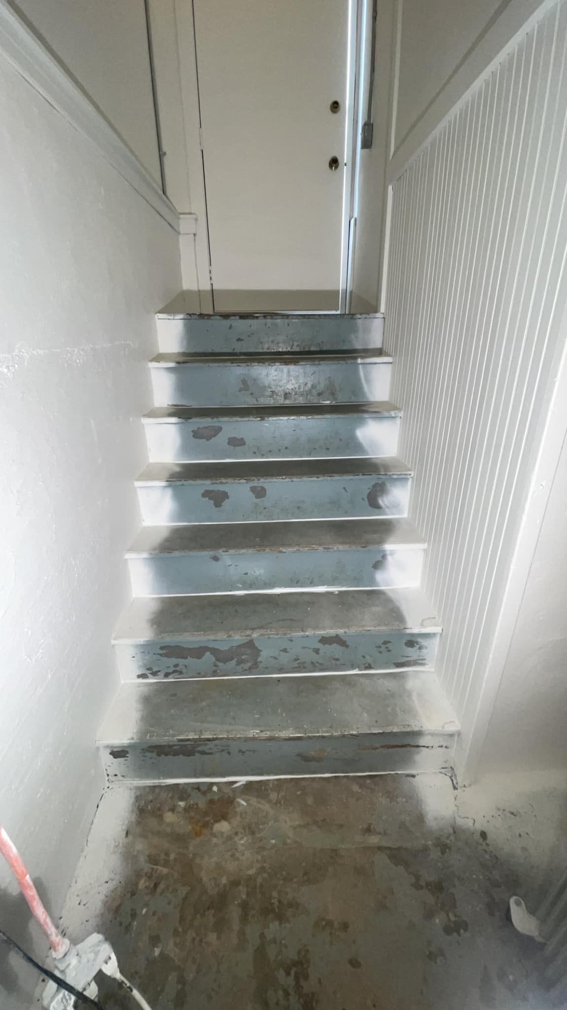 Staircase leading up with gray steps. Light and shadows are cast on the right wall. A door is at the top.