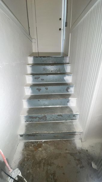 Staircase leading up with gray steps. Light and shadows are cast on the right wall. A door is at the top.