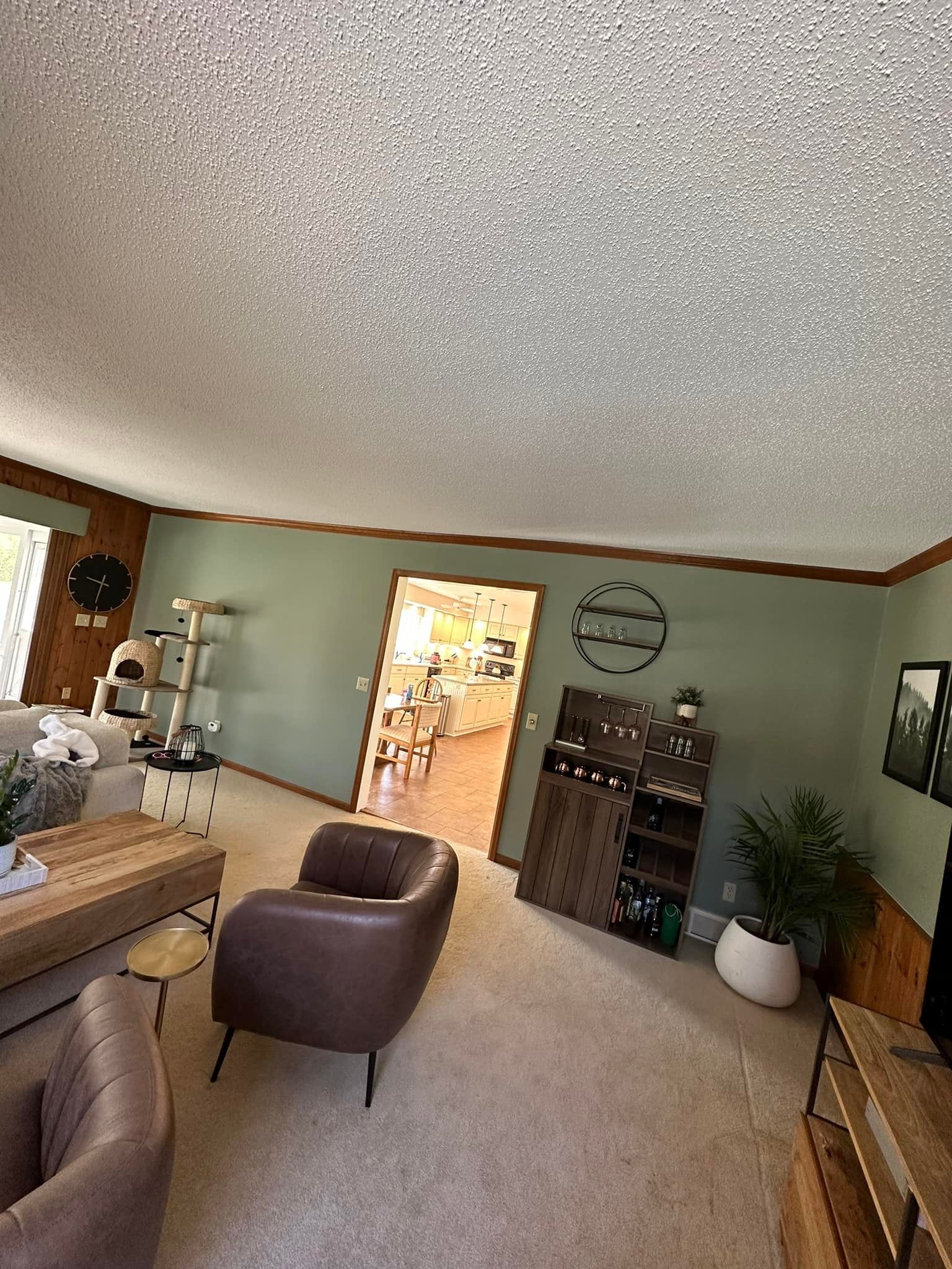 Living room with leather chairs, green walls, wooden bar cabinet, and doorway to kitchen.